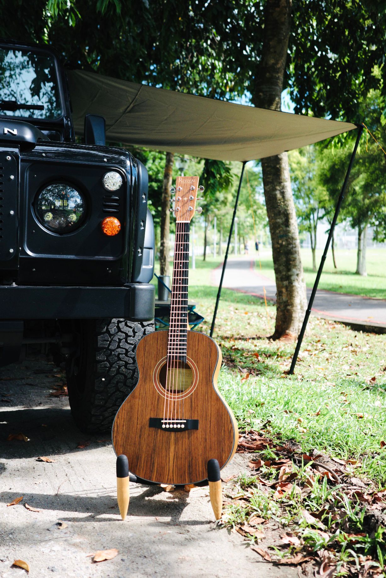 Revival Guitars travel acoustic leaning against a Land Rover Defender under a camp shelter